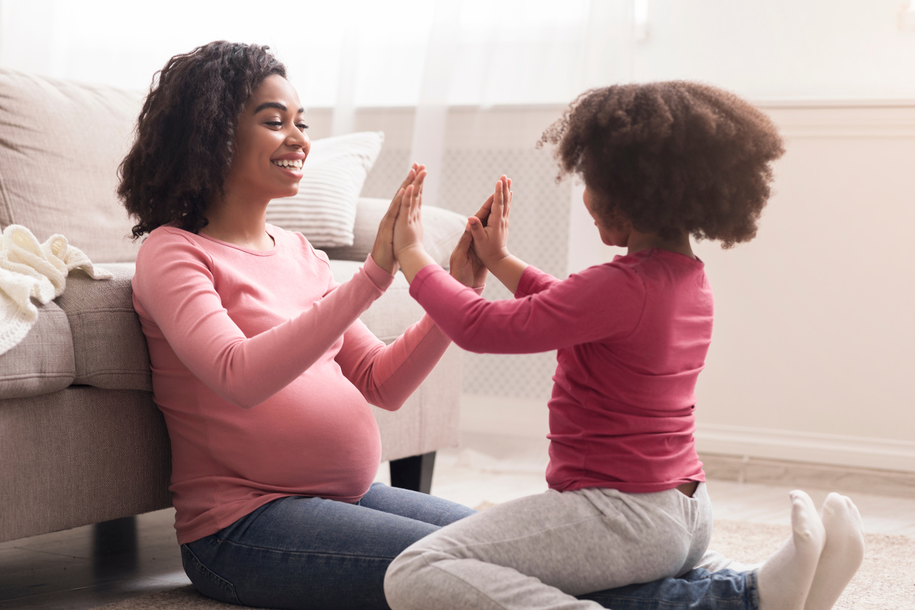 Happy little girl playing with pregnant black mom in living room